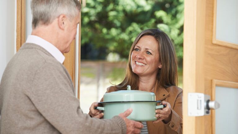A woman brings a casserole to a senior neightbor