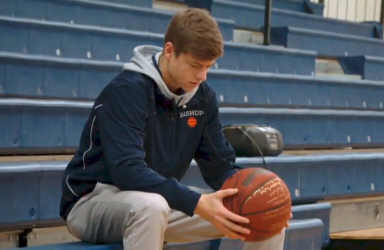 Teen sits on the bleachers holding a signed basketball.