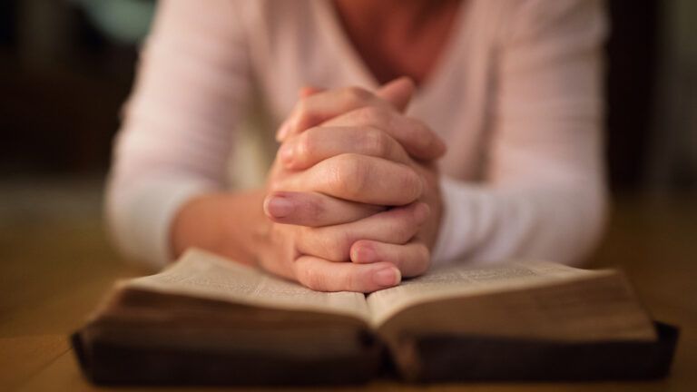 Woman praying with hands clasped together on her Bible. Close up.