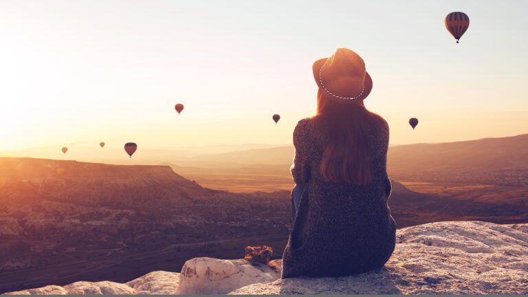 A woman on a hill gazes out at hot-air balloons in flight