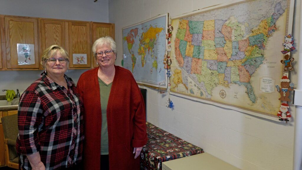 Two women in red stand next to the map for Santa's Letters